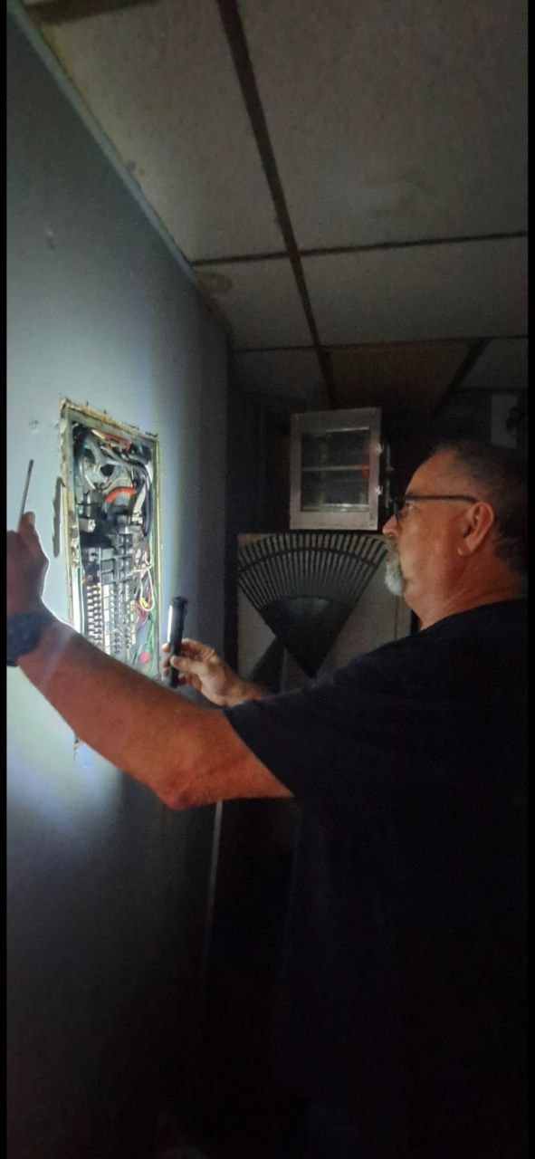 Inspector examining electrical panel interior with flashlight